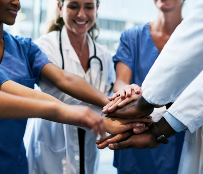 A team of healthcare professionals put hands together to symbolize teamwork.